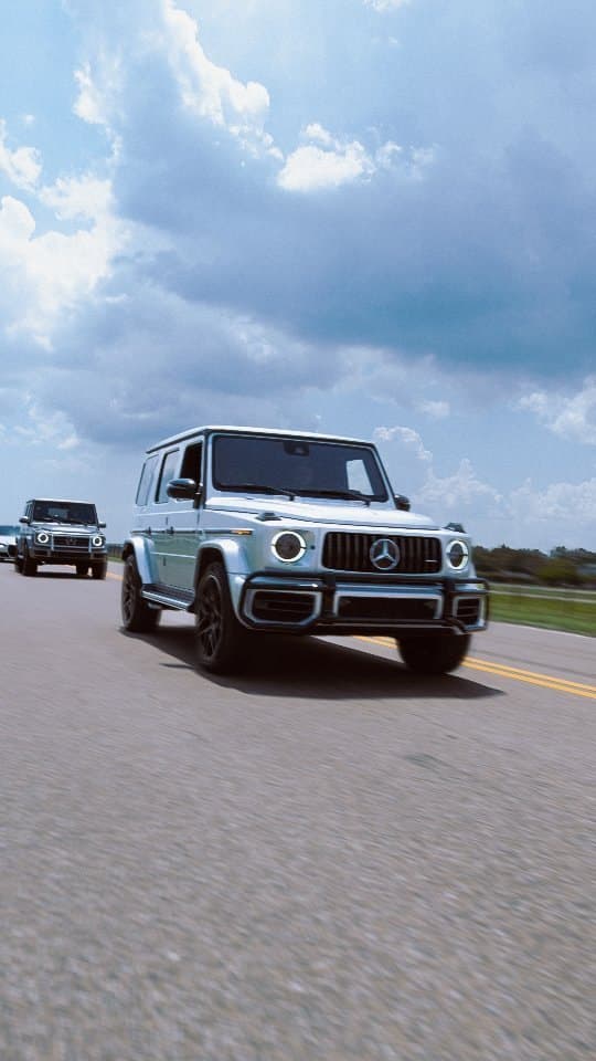 A silver Mercedes G-Class driving toward the camera on an open road