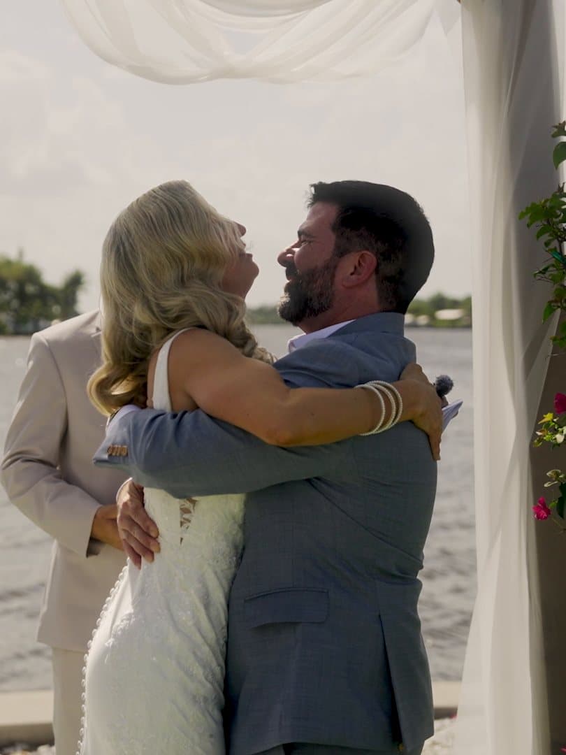 Andrea and Kevin embracing under the ceremony arch by the water in Fort Myers